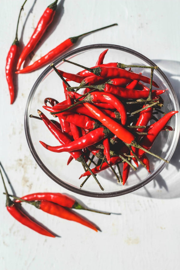 Red Thai chili peppers in a glass bowl on a white surface
