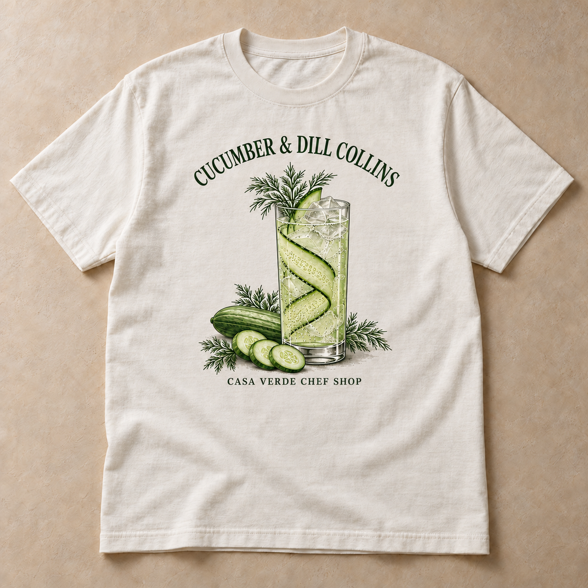 Cucumber & Dill Collins T-Shirt — approved individual front design preview with an illustrated Collins glass with a cucumber ribbon, cucumber slices and dill and the Casa Verde Chef Shop signature. Illustrative garment mockup, not a production master.