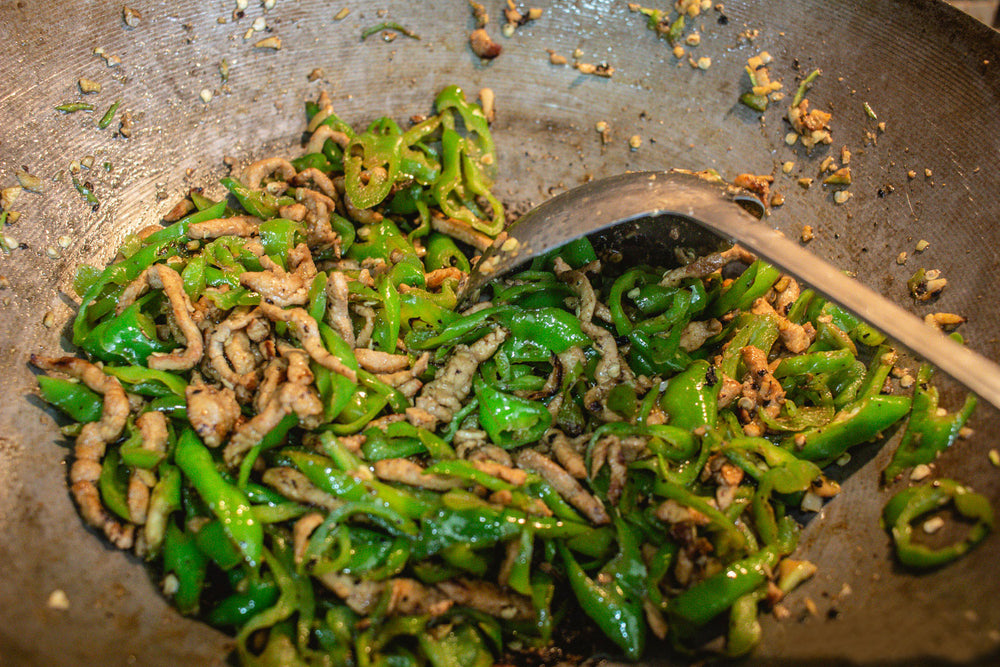 Stir-fried green fushimi peppers and meat in a wok with a wooden spoon.