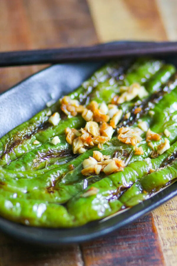 Grilled green Manganji peppers with garlic on a black plate on a wooden surface