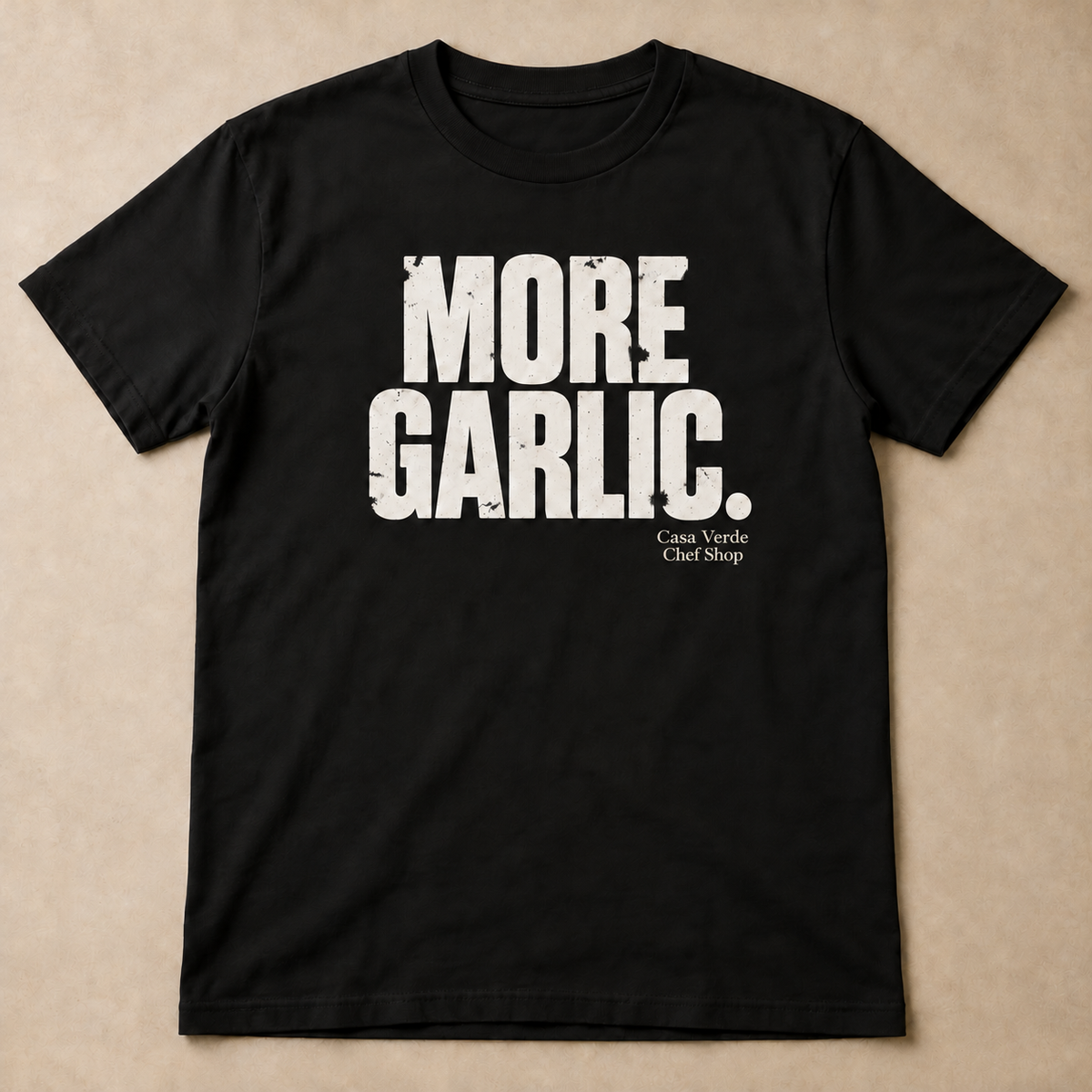Black T-shirt preview with distressed white MORE GARLIC. lettering on the front. With a small Casa Verde Chef Shop signature printed below the artwork. Design preview; final garment pending.