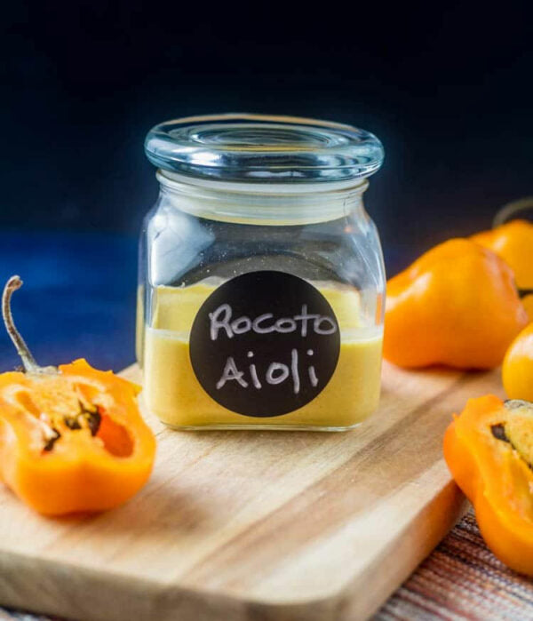 Jar of Rocoto Aioli on a wooden board with rocoto peppers