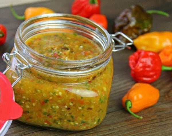 Jar of spicy sauce with peppers on a wooden surface