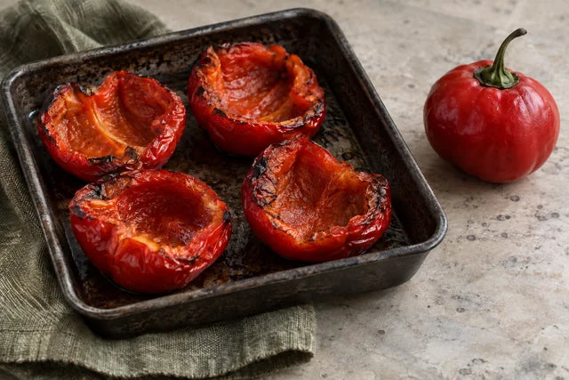 Culinary illustration of four roasted Rocoto Red pepper halves on a baking tray beside one whole red pepper